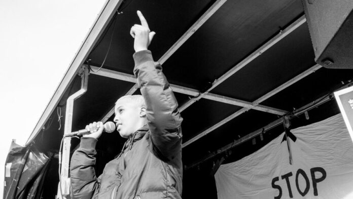 Primeira-ministra Mette Frederiksen fala em uma conferência de imprensa, em ambiente formal e iluminado.