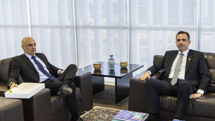 michelle-bolsonaro-e-alexandre-de-moraes-se-re-nem Michelle Bolsonaro e Alexandre de Moraes sentados em mesas separadas, mantendo postura formal em ambiente oficial.