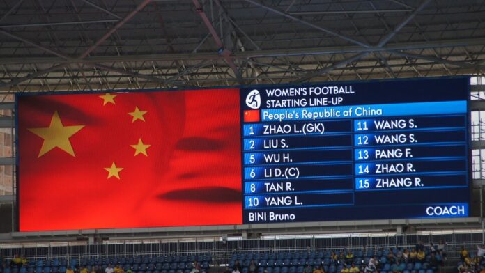 Jogadoras de futebol feminino em disputa de bola durante partida oficial em campo de gramado sob luz do dia.