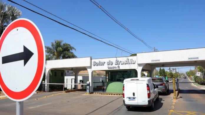 Drone sobrevoando área residencial cercada por grades metálicas e forte esquema de segurança policial.