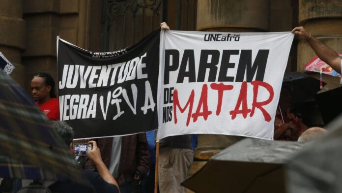 Manifestantes seguram cartazes e fotos em protesto contra a violência policial em frente a um prédio público em SP.