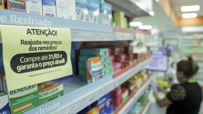 Prateleiras de supermercado com cartazes de farmácia ao lado de produtos de mercearia em um corredor amplo.