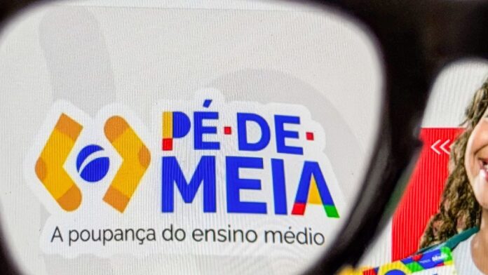 p-de-meia-2026-veja-as-datas-da-primeira-parcela-p Estudante segura um cartão bancário próximo a um computador, com interface de aplicativo de banco aberta na tela.