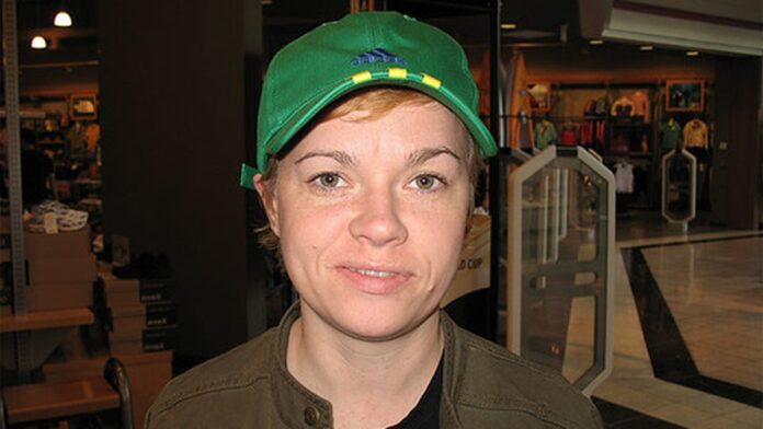 Profissional de saúde aplica vacina contra gripe em pessoa sentada em posto de atendimento com cartazes de campanha.