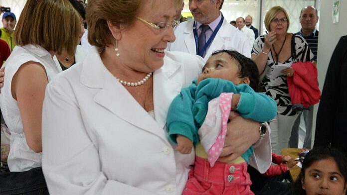 Profissional de saúde, usando fone de ouvido, realiza atendimento por videochamada em um monitor para um paciente.