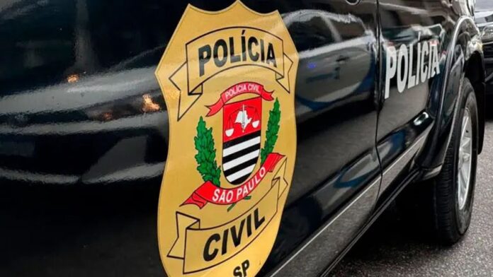 Agentes da Polícia Civil de SP em operação, vestindo coletes táticos, durante busca de documentos em escritório.