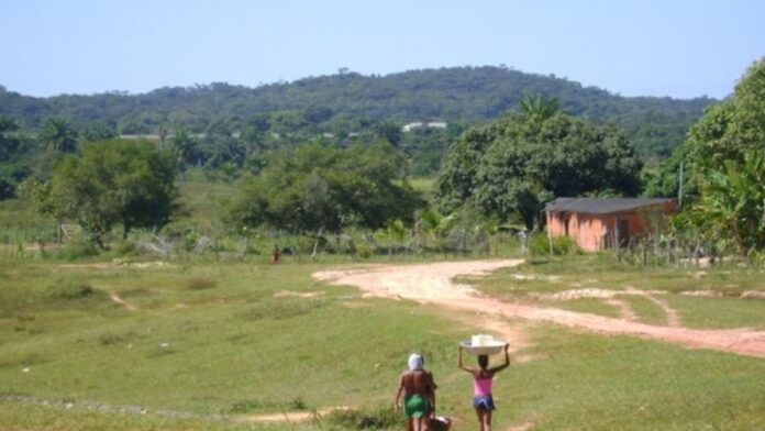 Família quilombola sorridente em área rural de Pernambuco, com vegetação ao fundo e símbolo do Incra em destaque.