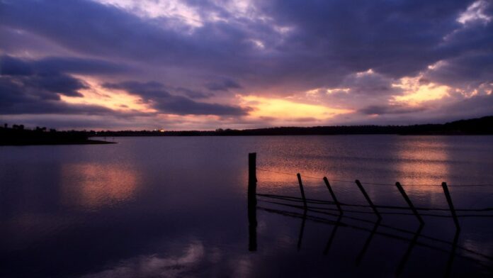 Sol forte brilhando sobre céu azul com nuvens carregadas e escuras no horizonte, indicando mudança climática.
