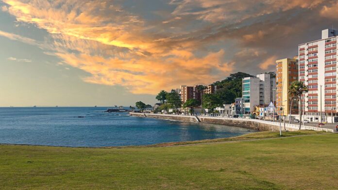 Mão segurando um smartphone moderno sobre uma superfície de madeira, com gráfico de desvalorização ao fundo.