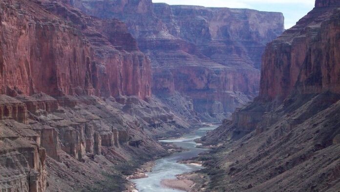 Vista aérea do leito do rio Colorado com baixo nível de água e margens secas e rachadas sob céu claro.