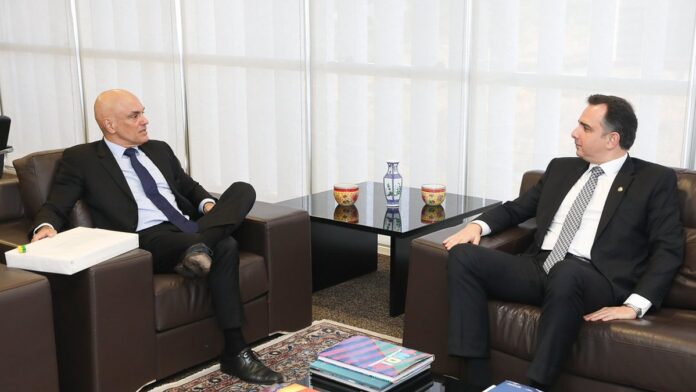 Rodrigo Pacheco discursa em evento solene, posicionado atrás de um microfone com bandeiras do Brasil ao fundo.