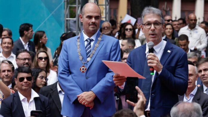 Romeu Zema cumprimenta o vice-governador Mateus Simões durante cerimônia de transmissão de cargo em Minas Gerais.