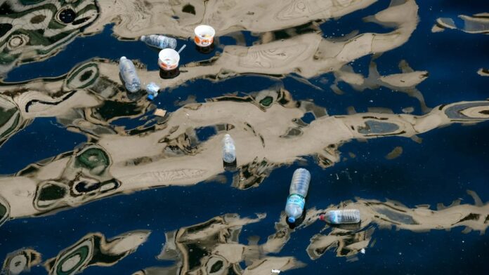 Floating plastic bottles and trash polluting a waterway with reflections.