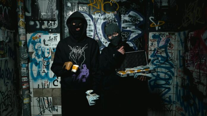 Two masked individuals with money in a graffiti-covered room, suggesting themes of crime and anonymity.