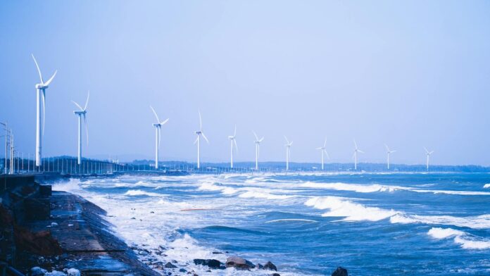 Picturesque view of a coastal wind farm with turbines and waves under a clear blue sky.