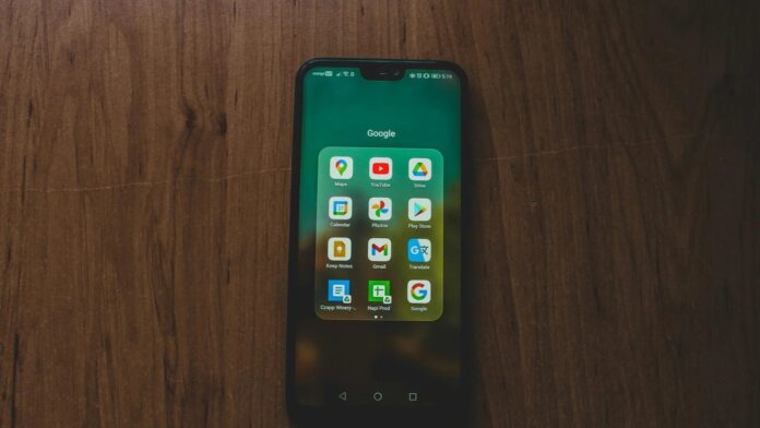 A smartphone showcasing various Google apps on a wooden table.