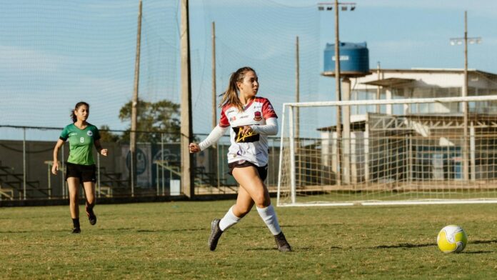 Two women soccer players in action on a grassy field under sunny conditions.