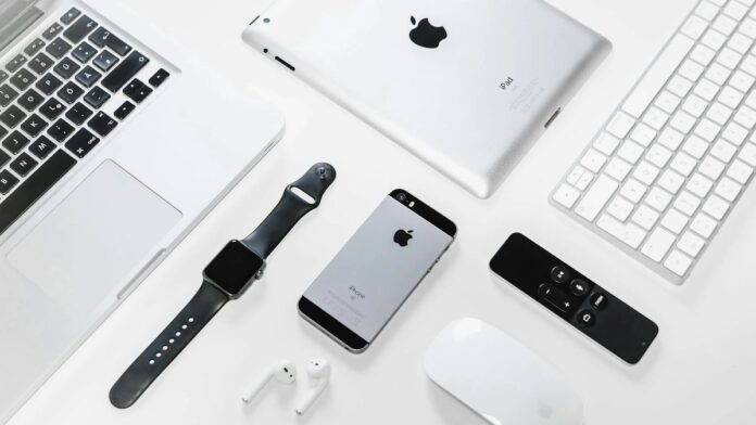 Flat lay of Apple devices including iPhone, iPad, MacBook, and Watch on a white surface, ideal for tech enthusiasts.