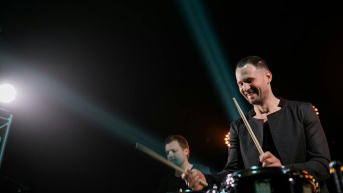 Energetic live concert shot featuring drummers playing on stage with vibrant lighting.