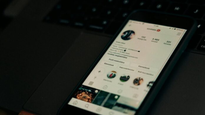 Close-up of smartphone showing a social media profile screen next to a laptop.