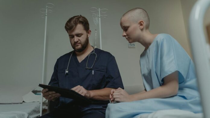 Doctor consulting with a young patient in a hospital room using a digital tablet.