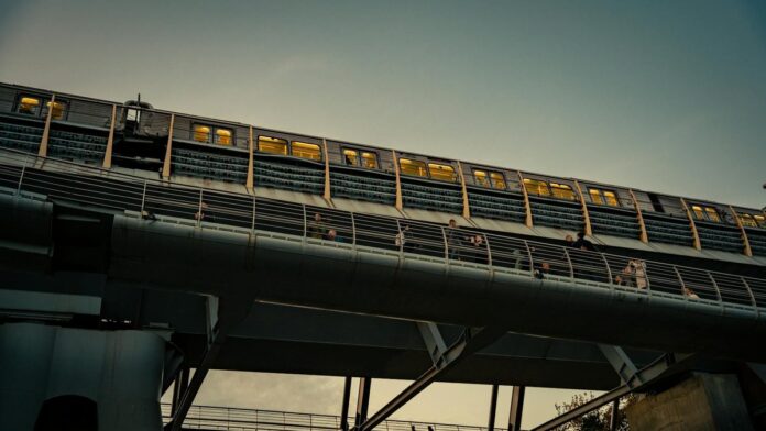 s4-badd19d005aa-1 City train crosses an elevated bridge at sunset with people walking below. Urban transit scene.