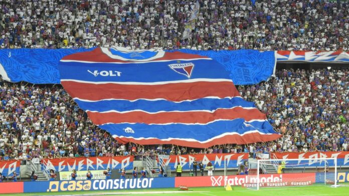 Large Fortaleza shirt banner held by fans in a bustling stadium.