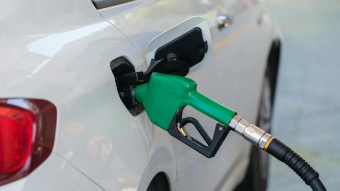 Close-up of a green nozzle refueling a white car at a gas station.