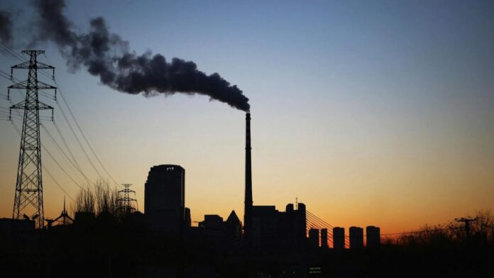 Dramatic sunset silhouette of an industrial smokestack with pollution in the urban skyline.
