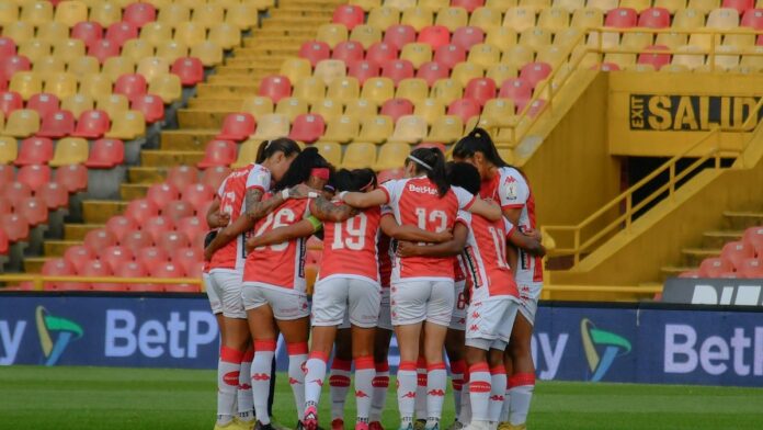 A women's soccer team grouped together in a huddle on the field before a match.