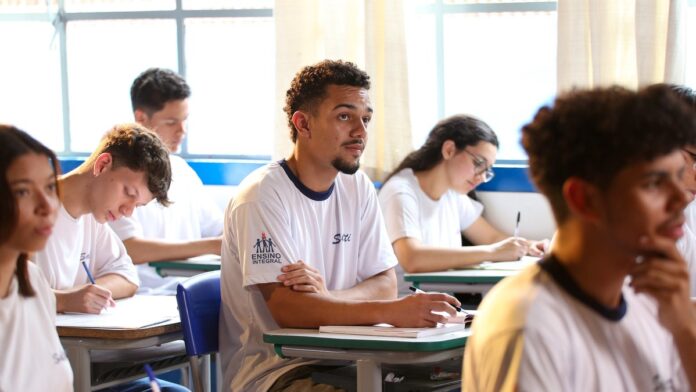 Estudantes sentados em carteiras escolares respondendo a uma prova de matemática em uma sala de aula.