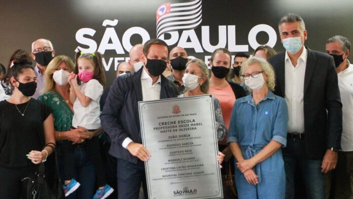 Policial conduz homem algemado em corredor, sob escolta, durante operação de prisão.