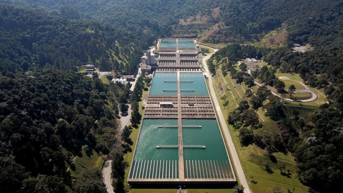 Vista aérea de uma grande estação de tratamento de água com tanques circulares e tubulações em São Paulo.
