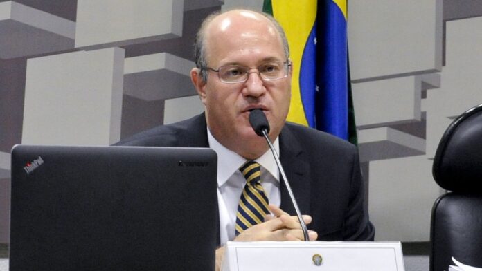 Multidão em show ao ar livre à noite, com palco iluminado, luzes coloridas e artistas se apresentando.