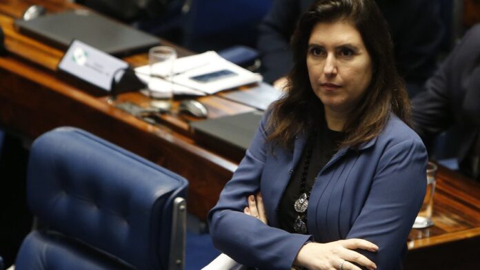 simone-tebet-confirma-filia-o-ao-psb-para-disputar Simone Tebet sorri e acena para apoiadores em evento de filiação partidária, vestindo roupa social em ambiente interno.