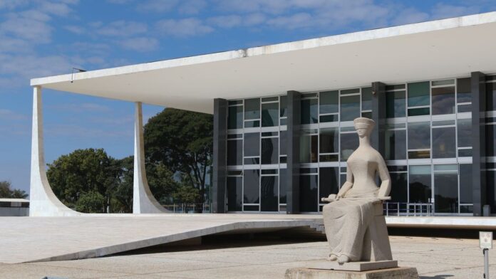 Fachada do prédio do Supremo Tribunal Federal, com colunas monumentais e a bandeira do Brasil ao fundo.