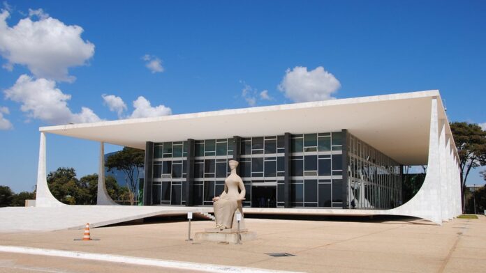 Fachada do prédio do Supremo Tribunal Federal, com colunas curvas e bandeira do Brasil hasteada ao fundo.
