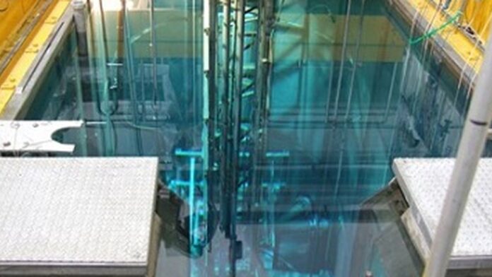 Fachada do prédio do Ipen com tubulações e estruturas metálicas em destaque, sob céu nublado.