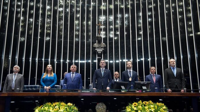 Foto de um tribunal com um homem sentado à mesa, pensativo, olhando para papéis e um computador.