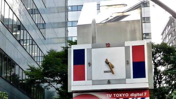 Donald Trump ao microfone em palanque, com bandeira dos EUA ao fundo e expressão séria.