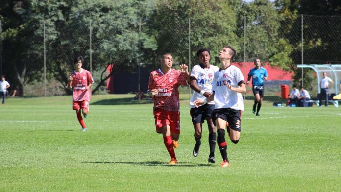 Jogadores de futebol em campo durante partida profissional, focados na disputa de bola em estádio iluminado.