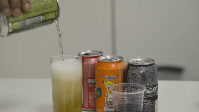 Criança segurando pacote de salgadinho industrializado em mesa com outros alimentos ultraprocessados.