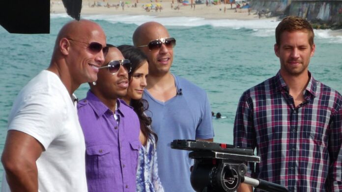 Roteirista em reunião de produção com pôster da franquia ao fundo.