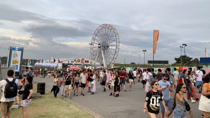 Multidão de jovens aguarda embarque em plataforma de trem decorada com as cores do festival Lollapalooza.