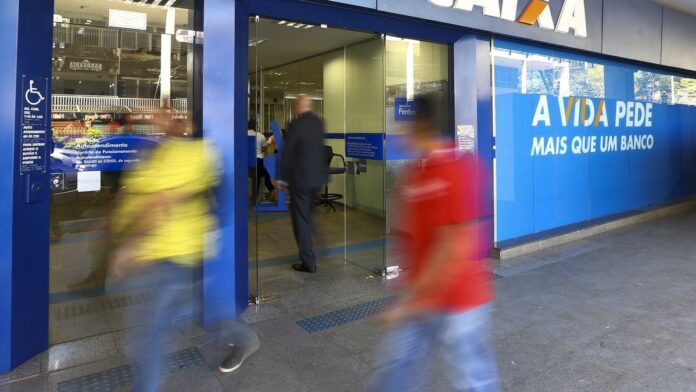Fachada de agência bancária com portas de vidro fechadas e aviso de expediente suspenso em feriado.