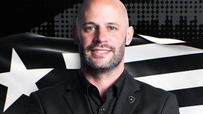 Foto de Franclim Carvalho, novo técnico do Botafogo, sorrindo e vestindo agasalho oficial do clube.
