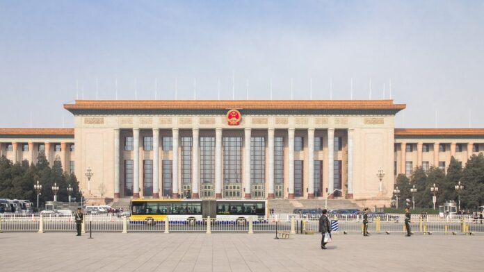 Fachada de um tribunal chinês com bandeiras nacionais ao fundo e cercas de metal em primeiro plano.