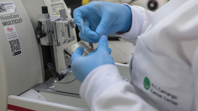 Médico opera braços robóticos em console cirúrgico de alta tecnologia com tela exibindo detalhes do procedimento.