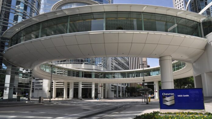 Ilustração de mãos de crianças folheando livro colorido sobre energia, com ícones de óleo e símbolos de reciclagem.