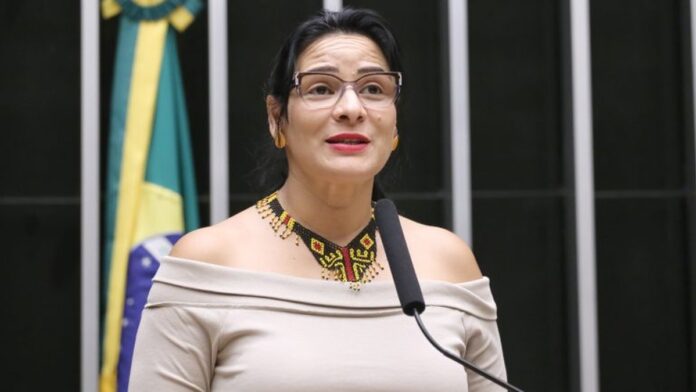 Representantes de povos indígenas discursam em plenário lotado na Câmara dos Deputados, com uso de adereços tradicionais.